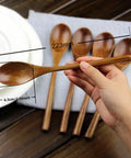 Hand holding spoon from Six Piece Japanese Natural Wooden Spoons Set For Cooking And Eating Great For Stirring Tea Honey Soda Dessert And Nonstick Pots Made From Nanmu Wood About Eight Point Seven Eight Inches Long Eco Friendly Kitchen Tools.