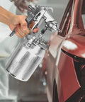 Hand holding Suction Type Paint Spray Gun With 2.0mm Nozzle near car for auto body painting and repair.