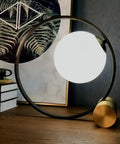 Mid Century Modern Nightstand Lamp In Black Matte Metal With Frosted Glass Globe illuminating on a wooden desk with decor.