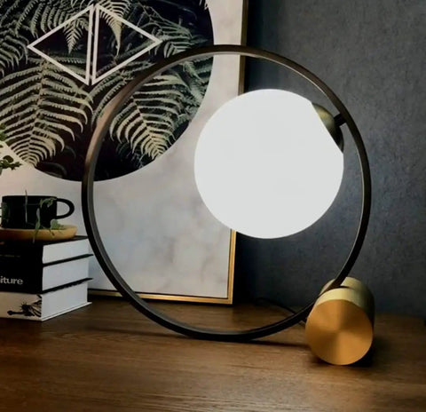 Mid Century Modern Nightstand Lamp In Black Matte Metal With Frosted Glass Globe illuminating on a wooden desk with decor.