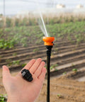 Hand holding 20 Pack Drip Irrigation Air Release Valve with farm irrigation setup in background.