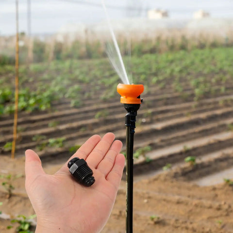 Hand holding 20 Pack Drip Irrigation Air Release Valve with farm irrigation setup in background.