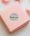 Pink gift box with a Thank You Stickers For Packaging And Gift Wrapping, Sturdy Copper Plate Self Adhesive Sealing Labels on top.