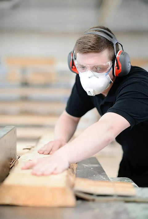 Man wearing overhead hearing protection ear muffs with 28 decibels NRR in a woodworking environment for comfort and safety.