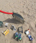 Heavy Duty Garden Rake That Slays Leaves And Debris With Ease showing red handle and sturdy tines on sandy ground with trash