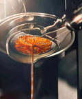 Close-up of espresso pouring from 58mm brew head of hand cranked espresso machine, showcasing rich crema for silky lattes.