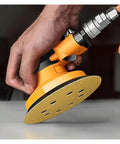Hand holding a 5 inch orbital sander with a yellow hook loop sanding disc, showcasing fast dust extraction for smooth polishing.