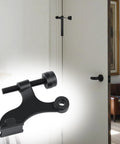 Built Tough Zinc Hinge Pin Door Stops Adjustable Matte Black Finish With Plush Bumper Caps To Save Drywall And Hardwood Floors Effortless Drop In Installation Eight Pack No Drama Setup mounted on a door frame.