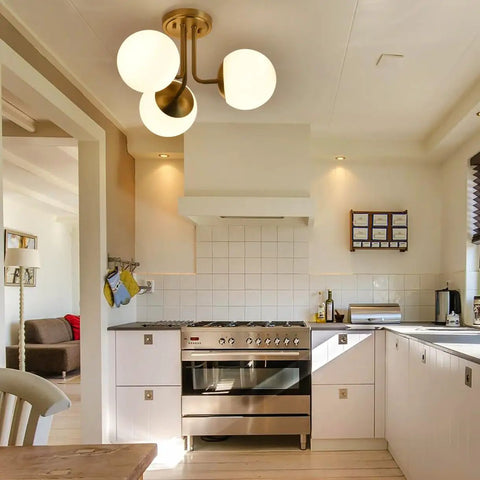 Three Light Aged Brass Semi Flush Mount Ceiling Light Fixture With White Globe Glass in modern kitchen setting