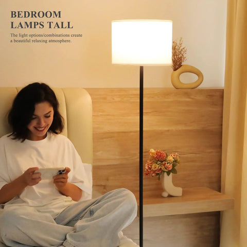 Floor lamp with black metal pole and white fabric shade, 60-inch tall, shown beside a person sitting on a bed.