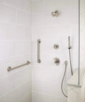Modern shower with stainless steel fixtures, including grab bars, handheld showerhead, and controls on tiled wall.