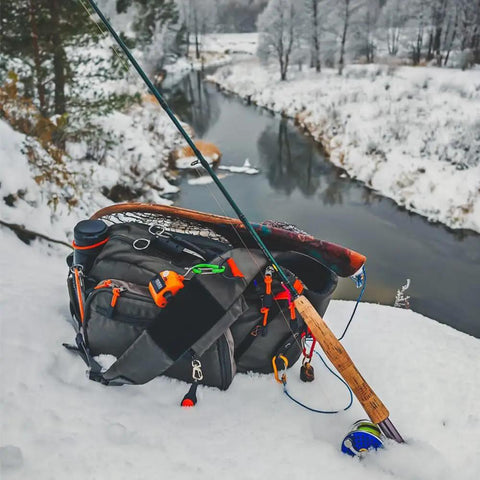 Fly Fishing Sling Pack For Quick Access Tackle Storage Shoulder Bag With Adjustable Padded Straps next to fishing rod in snow