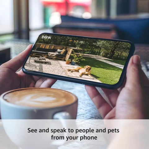 Hands holding a phone showing the Outdoor 4 Wireless Security Camera System With Two Year Battery Life, 1080p HD Live View of a garden.
