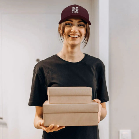 Person wearing Its My Birthday Trucker Hat Unisex Cool Baseball Cap, adjustable, holding gift boxes, smiling indoors.