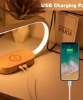 Wooden Bedside Lamp With Wireless Charger And Clock Touch Nightstand Lamp with USB charging port next to a charging smartphone.