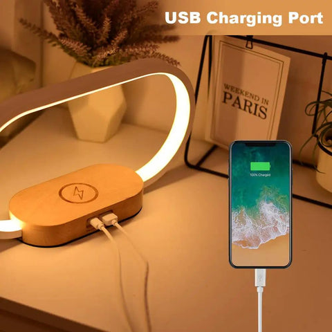 Wooden Bedside Lamp With Wireless Charger And Clock Touch Nightstand Lamp with USB charging port next to a charging smartphone.