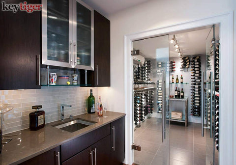 Modern kitchen with glass door leading to wine storage with wooden cabinets and metal shelving, integrated lighting