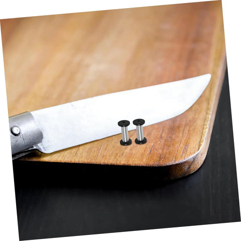 Badass Flat Head Knife Handle Screws And Brass Snap Rivets For Wood And Metal Crafts Tight Fit 2 Piece Kit on a wooden cutting board.