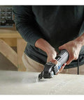 Man using 5 Amp Tool-Less Oscillating Tool Kit With Accessory Set For Cutting Sanding Grinding And Scraping on wooden board