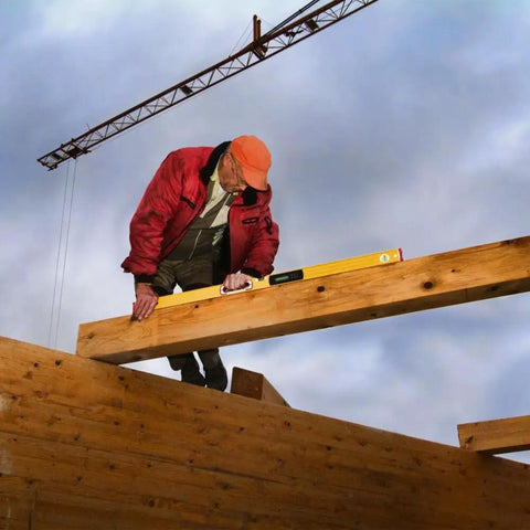 Worker using 48 Inch Type 196-2 Digital Tech Level Tool Boasting Dead Nuts Electronic Vials on a wooden beam at a construction site.