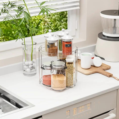 Totally Slick No Hassle 360 Spin Vanity Organizer Two Tier Clear Acrylic Rotating Storage For Perfume And Lotion Lazy Susan Beauty Stand Keeps Skincare Fully Within Reach On Any Desk displayed on a kitchen countertop with jars and a plant.