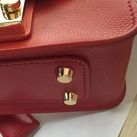 Close-up of Straight Up Solid Brass Purse Feet With Flat Head Studs on a red leather handbag, emphasizing shiny finish and sturdy design.