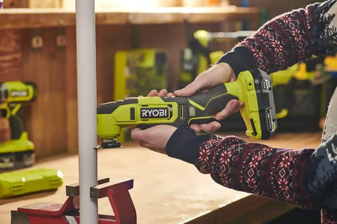Person using Built Different 18V Cordless Multi Tool to cut a white pipe in a workshop, showcasing its versatility and precision.