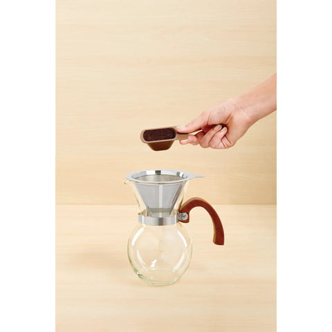 Next Level Pour Over Coffee Maker With Heat Resistant Borosilicate Glass Carafe And Comfortable Bamboo Handle Plus Durable Stainless Steel Filter For Killer Black Coffee And Straight Up Smooth Sips Daily with coffee grounds being added.