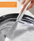Stainless steel kitchen whisk held by hand above a foamy pot of soapy water.