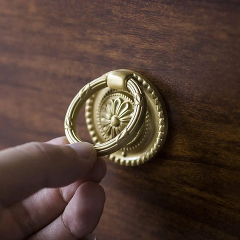 Hand grasping Brass Cabinet Ring Knobs Set, Gold Round European Style Drawer Pulls on wood surface