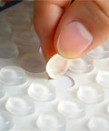 Close-up of a hand peeling a silicone pad from a sheet, part of Bulk 1000 Pack Silicone No Slip Pads For Drawers And Cabinets.