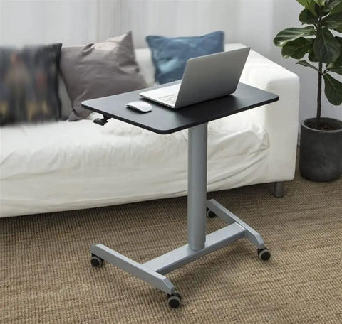Smooth Roll Mobile Standing Desk With Height Adjustable Pneumatic Lift Sleek Black Aluminum Frame Ergonomic Rolling Workstation beside a couch, laptop and mouse on black surface.