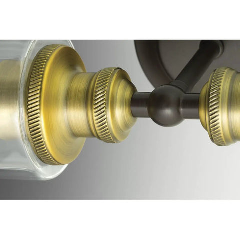 Close-up view of Two Light Clear Glass Farmhouse Bath Vanity Light in Antique Bronze Finish with warm ambient lighting details.