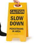 Person holding Caution Slow Down Pedestrians In Area Folding Floor Sign 25 By 12 Inches Plastic Black On Yellow Big And Bright Double Sided Durable Sign With Easy Carry Handle For Indoor Or Outdoor Use.