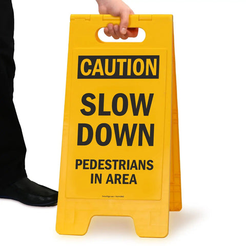 Person holding Caution Slow Down Pedestrians In Area Folding Floor Sign 25 By 12 Inches Plastic Black On Yellow Big And Bright Double Sided Durable Sign With Easy Carry Handle For Indoor Or Outdoor Use.