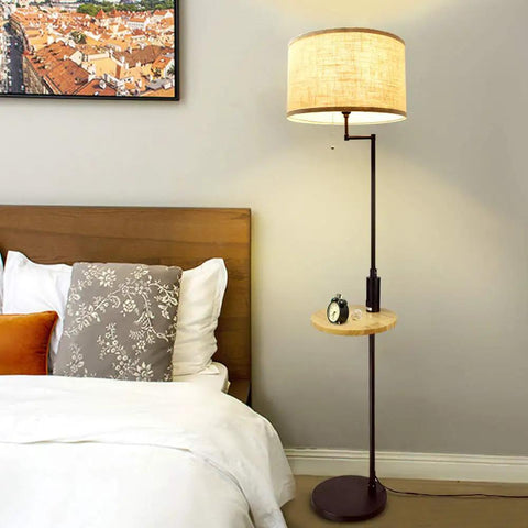 Bedroom with a standing floor lamp beside a bed, featuring a wooden mini-shelf and beige lampshade, modern decor style.