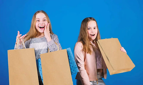 Two girls holding Bulk 500 Pack Heavy Duty Kraft Paper Bags 10x13 Inches With Handles, looking surprised.