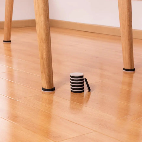 Round 2 Inch Felt Furniture Sliders Pack 24 Piece Heavy Duty Reusable Moving Pads For Sofas And Tables Easy Glide On Hardwood Floors Vinyl Ceramic Tile And Linoleum Non Stick Protection For Heavy Furniture on hardwood floor with some pads installed on chair legs and a stack of sliders in the foreground
