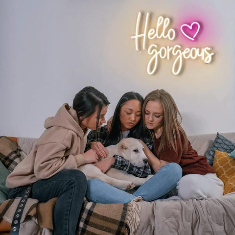 Hello Gorgeous Neon Sign For Girls Bedroom Wall Decor LED Light With Warm White Glow Perfect For Birthday Parties Weddings And Gifts 16.7x12.3 Inches Great Gift Idea illuminated above three people sitting on a couch with a dog.