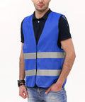 Man wearing blue safety vest with reflective tape, hands in pockets. Not related to 10 Pack Hi Visibility Safety Vests For Adults With Reflective Tape Bright Orange Color Breathable Lightweight Construction Workwear For Men And Women.