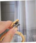 Close-up of a hand holding a khaki ring and clip, part of 2 Pack Curtain Rings With Clips Anti Slip Shower Drapery Hooks For Stable Curtain Suspension And Smooth Glide Rod Round Design Easy Install Durable No Snag.