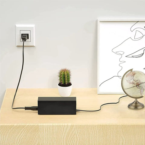 12V AC Power Adapter For Korg KROME EX 61 Key Music Workstation Keyboard Charger on table, plugged in, next to cactus plant
