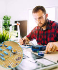 Electronics hobbyist soldering at a workbench; circular inset shows blue axial resistors from a resistor kit.