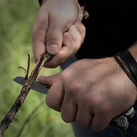 Person using 13 In 1 Stainless Steel EDC Multitool With Nylon Sheath For Camping, Hiking, And Fishing to cut a branch with knife blade