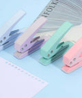 Set of colorful handheld paper punchers on blue background next to punched paper and magazines for DIY crafts and tags.
