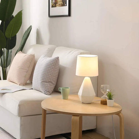 Modern White Ceramic Table Lamp With Irregular Geometric Base And White Fabric Shade Compact Nightstand Bedside Lamp For Bedroom Living Room Or Office 15 Inch Tall 7 Inch Diameter Sleek Decor Accent on round wooden table next to sofa