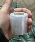 Hand holding a compact Stretchable Shrink Film Roll for Bottled Packaging and Non-Heated Bottle Sealing Machine, portable design.