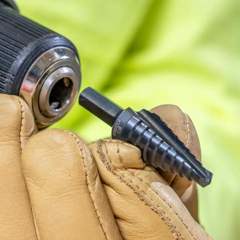 Gloved hand holding a Step Drill Bit Set With Double Flutes For Clean Cuts And Easy Read Markings, 1/4 To 3/4 Inch, 3/8 Hex Shank