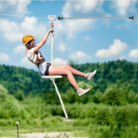 Person riding zipline with Extra Long Zipline Spring Brake For Backyard Kits, over green landscape.