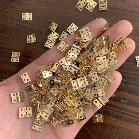 Hand holding a set of 1:12 scale miniature door hinges with screws, designed for dollhouse doors and cabinets, DIY projects, mini decor.